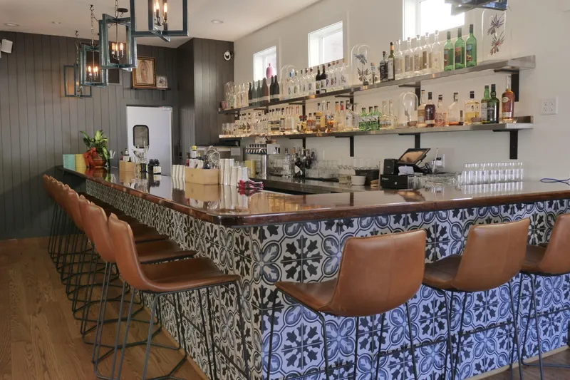Bar at Dolores in Providence with a blue-and-white Talavera-tiled counter, tan leather stools and shelves of agave spirits