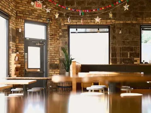 Interior of Donkey Taqueria in Grand Rapids: exposed-brick walls strung with papel picado stars, communal wood tables and stools, and an Avion tequila barrel