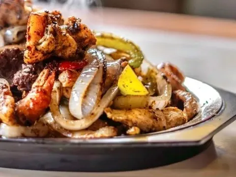 A sizzling cast-iron skillet of mixed shrimp, beef and chicken fajitas with grilled onions and peppers at Los Asaderos in Fort Worth