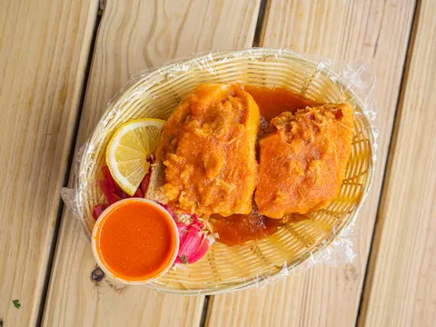 Two tortas ahogadas — birote rolls drenched in red chile sauce — in a basket with a cup of salsa, pickled onions and a lemon slice at Tortas Ahogadas El Chivito in San Antonio