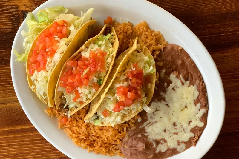 Plate of three crispy tacos topped with lettuce and diced tomato, served with Spanish rice and refried beans at Casa Corona in Fresno