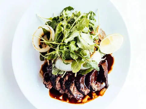 Plated grilled sliced steak with mole-style sauce, charred onion and arugula at El Barrio in Birmingham, Alabama