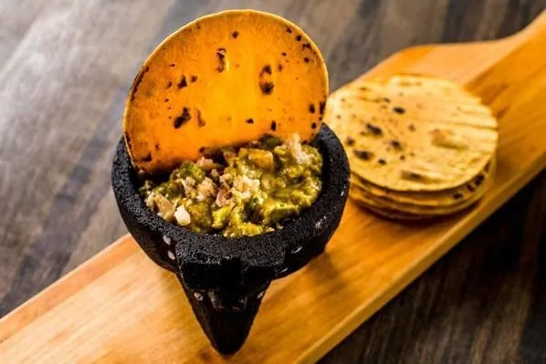 Smoked trout guacamole served in a stone molcajete with a toasted tortilla chip and stacked corn tortillas at Chavela's in Brooklyn