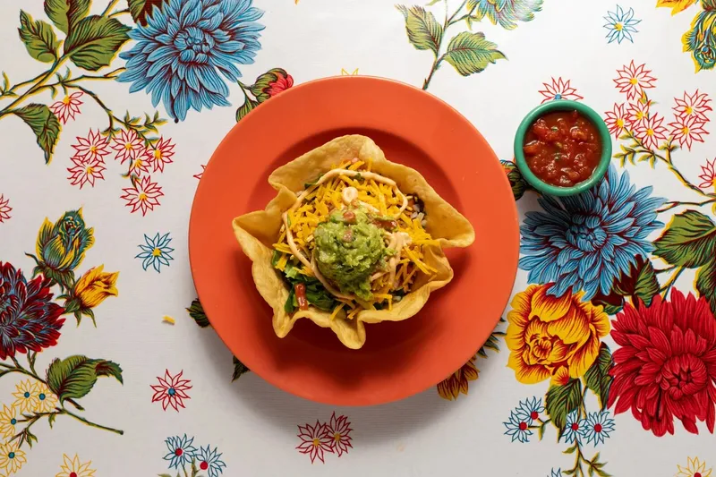 Taco salad in a tortilla bowl with guacamole and cheese beside a dish of salsa at Elote Cafe
