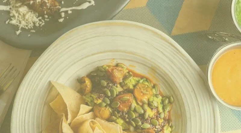 Overhead shot of a guacamole dish topped with pepitas at BelAir Cantina, served with tortilla chips and three salsas