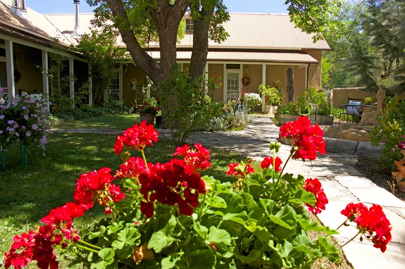 Flagstone courtyard with red geraniums leading to the historic adobe restaurant and hacienda at Rancho de Chimayó in Chimayó, New Mexico