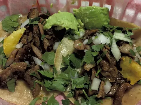 Two street tacos at Taco Gordo in Burlington, piled with grilled pork, chopped onion, cilantro, guacamole, and lime in a paper-lined basket