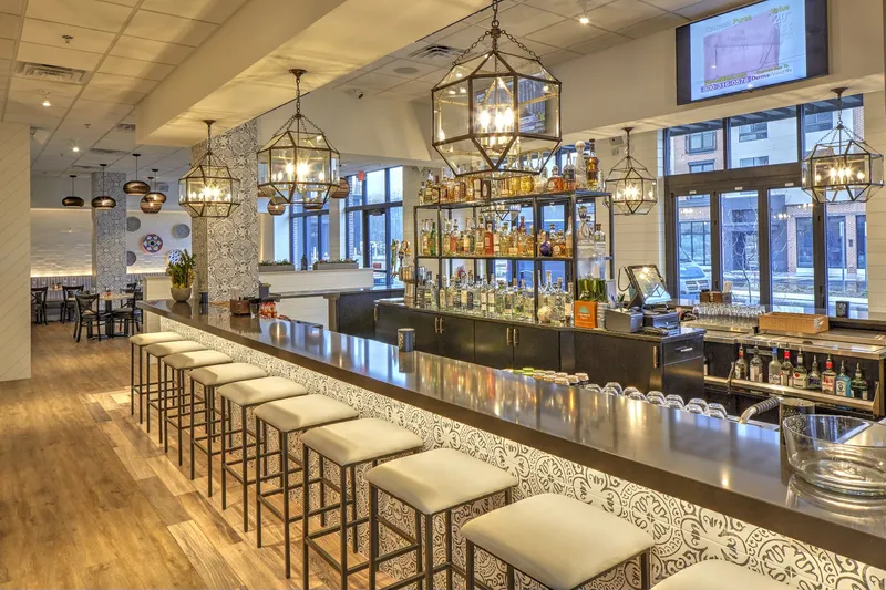 Interior bar at El Camino Mexican Kitchen in Wilmington, Delaware, with white barstools, patterned tilework and a lit back wall of tequila bottles